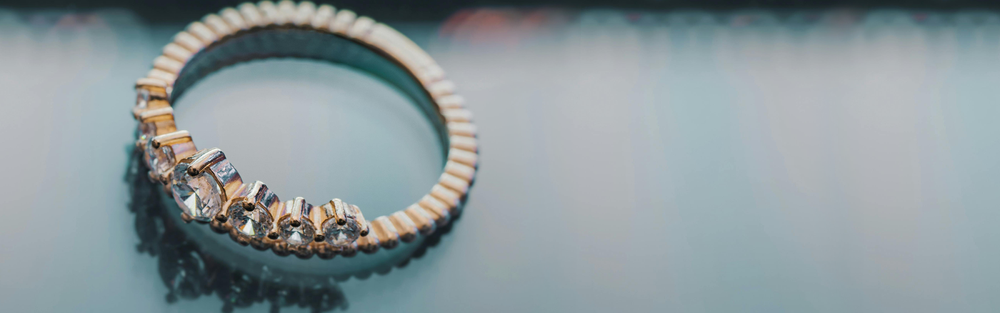 Close-up of a diamond-studded gold ring on a reflective surface.